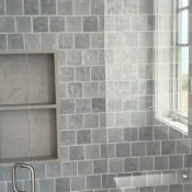 Finished blue-gray tile shower with a recessed shelf, brushed nickel shower hardware and a glass door