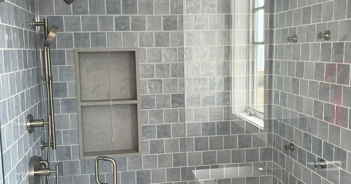 Finished blue-gray tile shower with a recessed shelf, brushed nickel shower hardware and a glass door