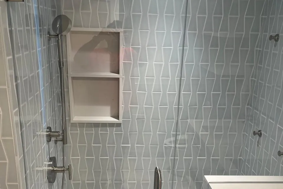 Glass-enclosed shower with angled blue-gray wall tile and recessed shelves