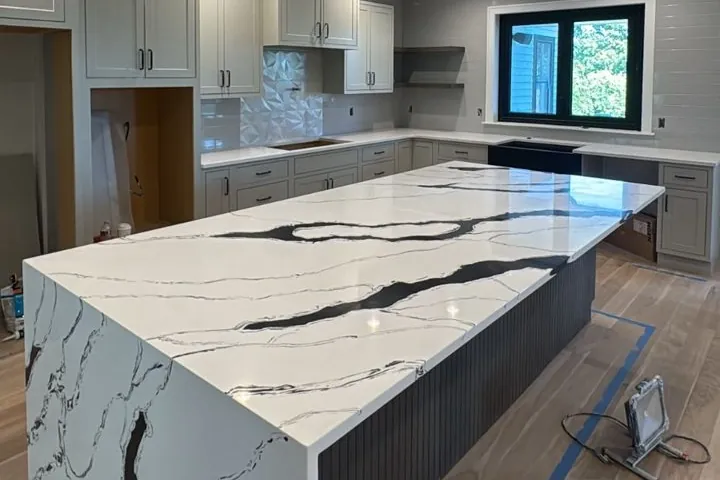 Kitchen with a waterfall quartz island, light cabinets and a light wood floor in the final stage of work