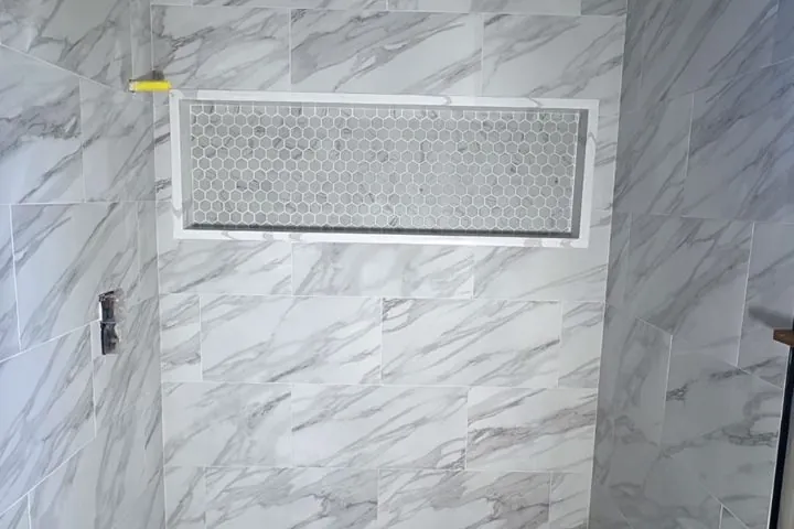 Shower wall in marble-look porcelain tile with a long hexagon mosaic niche