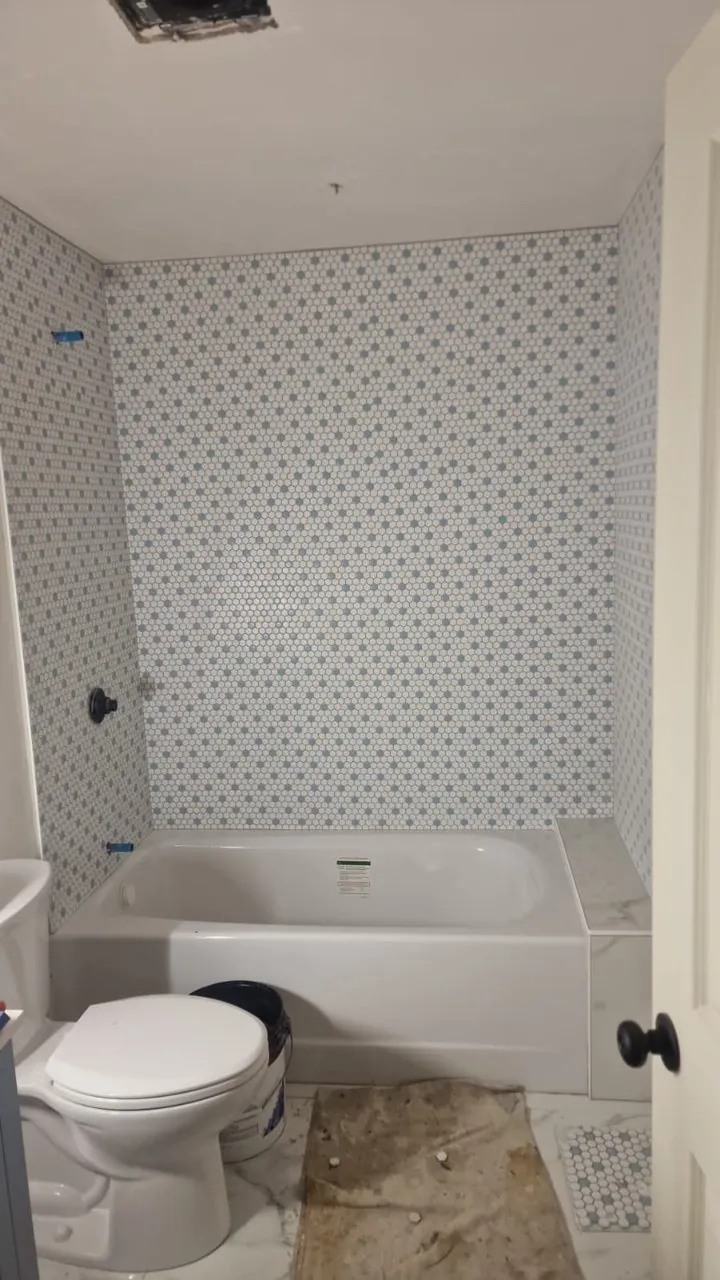 Bathroom with a new tub and a white mosaic tile wall, floor still unfinished during construction