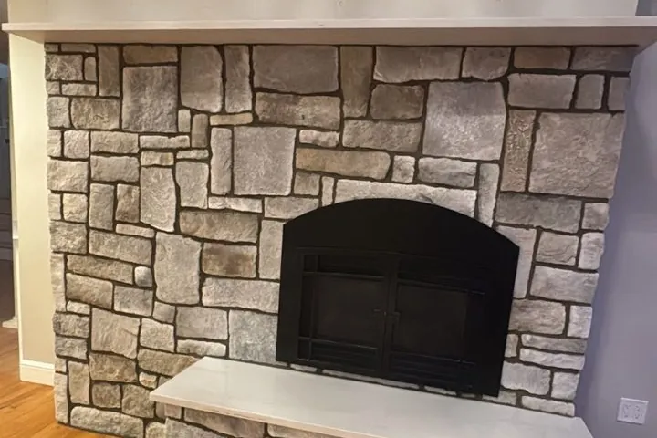 Stone-veneer fireplace surround with a black firebox and a light stone hearth