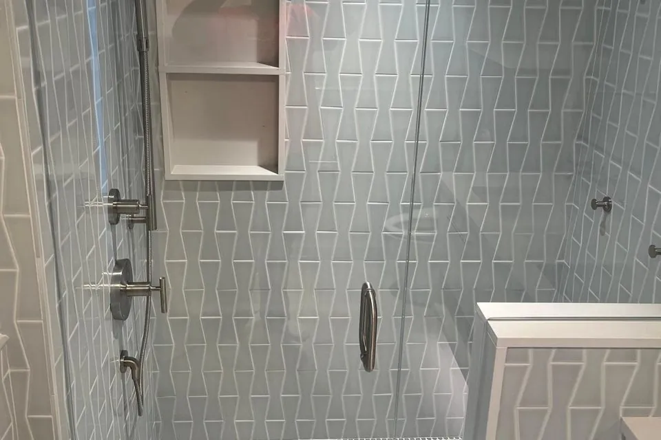 Shower wall in angled blue-gray tile with two recessed shelves and a glass door