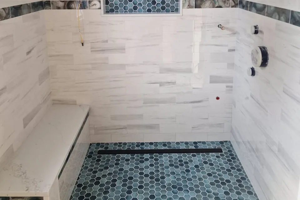 Large tiled shower with a built-in bench, a blue hexagon mosaic floor and a linear drain