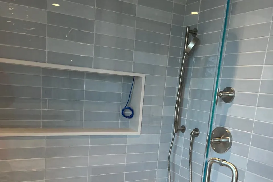 Walk-in shower wall with long blue-gray tile, a recessed niche and a handheld shower head