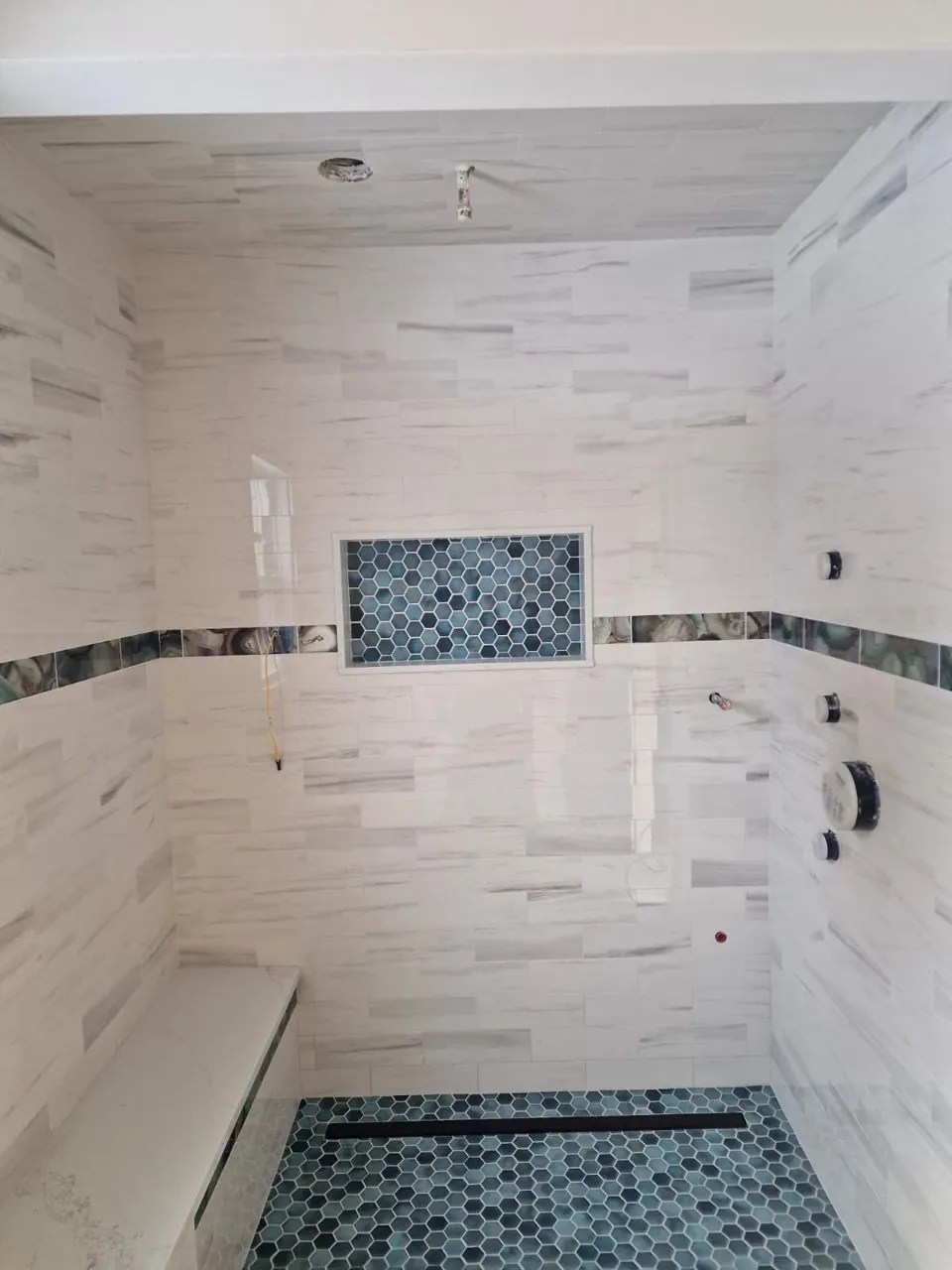 Walk-in tile shower with a built-in bench, a mosaic niche and a mosaic floor with a linear drain