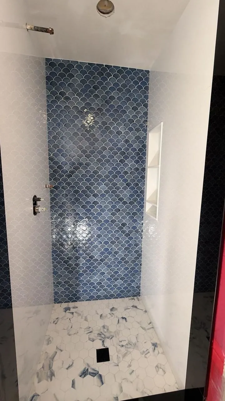 Blue fish-scale tile feature wall inside a shower lined with small white mosaic tile