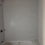 Small bathroom with a white alcove tub and a white and blue mosaic tile wall