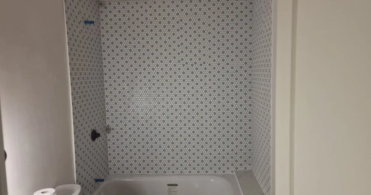 Small bathroom with a white alcove tub and a white and blue mosaic tile wall