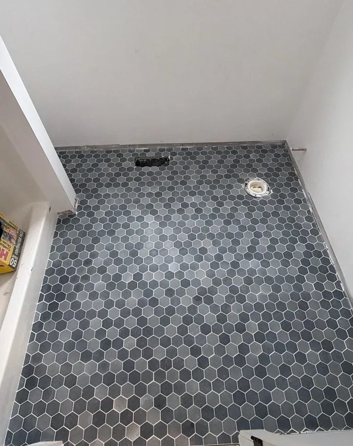 Blue-gray hexagon mosaic floor tile set wall to wall in a small bathroom before the toilet goes in