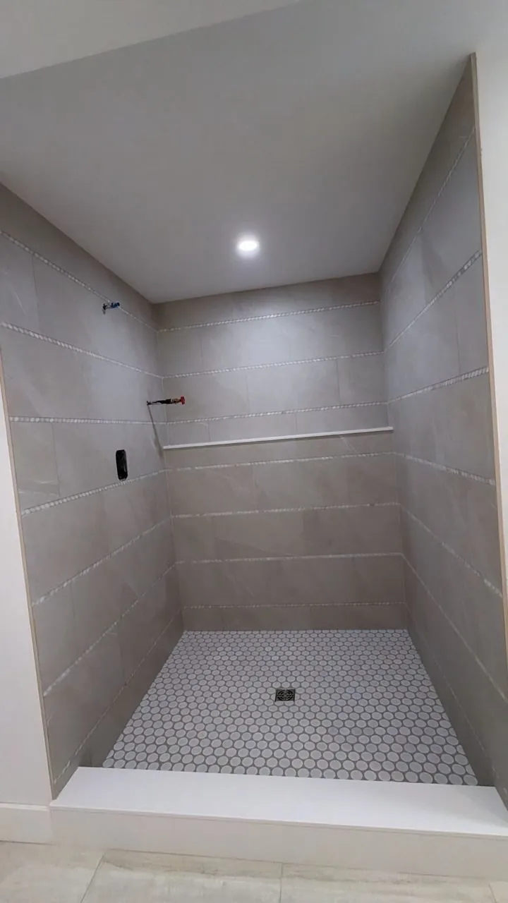 Shower with large gray porcelain wall panels and a small white hexagon mosaic floor under a recessed light