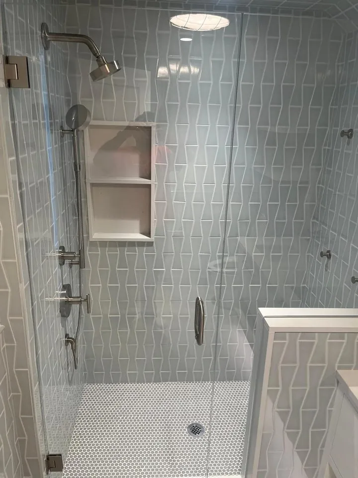 Two shelves recessed into a blue-gray tiled shower wall behind a clear glass door